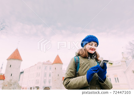 Tallinn, Estonia. Young Caucasian Woman Backpacker Tourist Enjoying Life, Smiling And Using Smartphone Near Landmark Viru Gate. Vacation In Old Town. Girl Surfing Net Internet In Phone 72447103