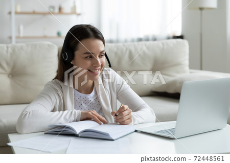 Smiling young woman in headphones looking at laptop screen 72448561