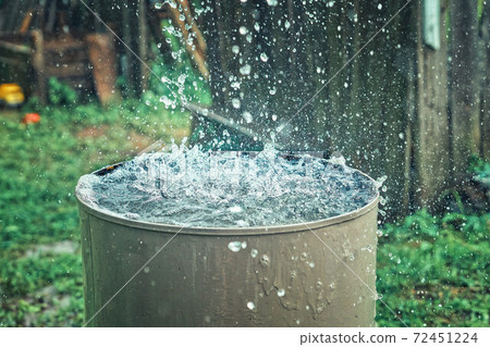Rain barrel. Strong stream of water pours into an old metal barrel during heavy rain 72451224