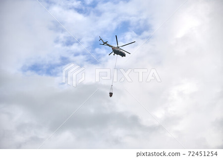 Fire fighting helicopter with water bucket on a cloudy sky background 72451254