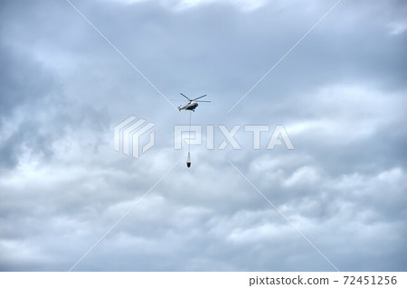 Fire fighting helicopter with water bucket on a gloomy sky background 72451256