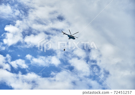 Fire fighting helicopter with water bucket on a cloudy sky background Fire fighting helicopter with water bucket on a cloudy sky background 72451257