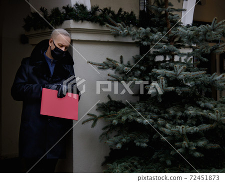 man in a black coat holds a red folder in his hands and watches the clock. man in a black coat holds a red folder in his hands and watches the clock. 72451873