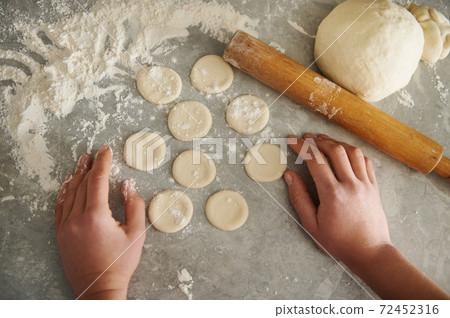 Cropped portrait of hands on the background of the dough on a table sprinkled with flour Cropped portrait of hands on the background of the dough on a table sprinkled with flour 72452316