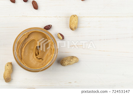 Jar of peanut butter on a white wooden table with nuts scattered nearby. Space for text. Jar of peanut butter on a white wooden table with nuts scattered nearby. Space for text. 72453147