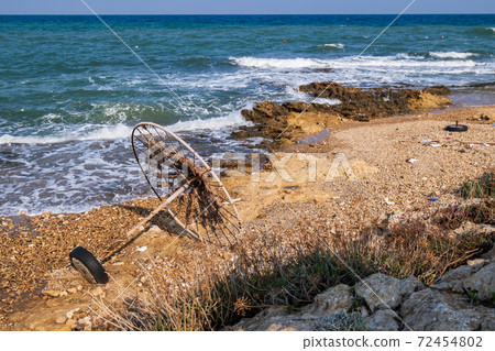Abandoned beach umbrella on a rocky beach set against the sea. 72454802