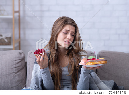 Depressed young lady having eating disorder, comforting herself with sweets on sofa at home 72456128