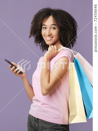 Portrait of african american female, holds colored shopping bags and phone and looking at camera Portrait of african american female, holds colored shopping bags and phone and looking at camera 72456646