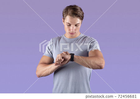 Strong athletic man looking at his smartwatch on violet studio background 72456681