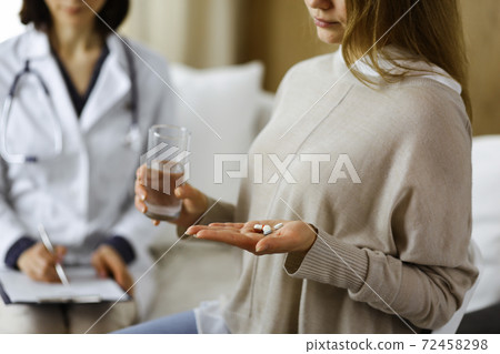 Close-up woman-patient holding pills near her doctor, time to take medications, cure for headache or remedy pain killer drugs. Stay at home concept during Coronavirus pandemic and self isolation Close-up woman-patient holding pills near her doctor, time to take medications, cure for headache or remedy pain killer drugs. Stay at home concept during Coronavirus pandemic and self isolation 72458298