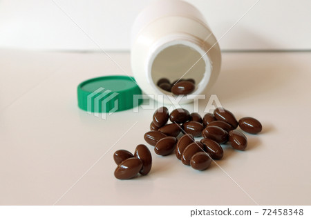 Pile of dark brown medicine on the white floor and white plastic bottle with green cap. 72458348