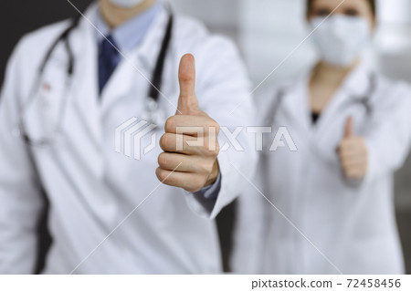 Unknown man-doctor and woman standing straight as a team and showing Ok sign with thumbs up in modern clinic. Medicine concept during Coronavirus pandemic. Covid 2019 Unknown man-doctor and woman standing straight as a team and showing Ok sign with thumbs up in modern clinic. Medicine concept during Coronavirus pandemic. Covid 2019 72458456