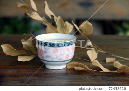 Tea in the cup with Dry branches and Leaves, light brown color on the wooden table.  72458626