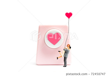 Miniature people couple hugging and holding balloon on white background 72458747