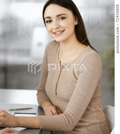 Young business people are talking to each other, while sitting at the desk in a modern office. Focus on woman. Concept of business success Young business people are talking to each other, while sitting at the desk in a modern office. Focus on woman. Concept of business success 72458808