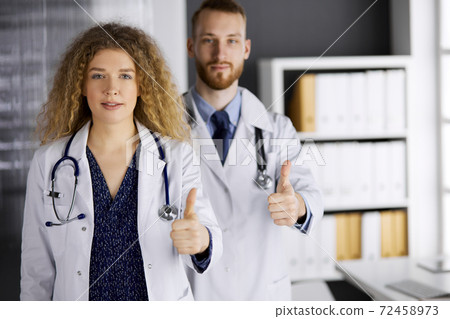 Two doctors standing with thumbs up in hospital office. Medical help, countering viral infection and medicine concept Two doctors standing with thumbs up in hospital office. Medical help, countering viral infection and medicine concept 72458973