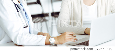 Unknown woman-doctor sitting and communicating with female patient. Physician checks medical history record and exam results, close-up. Healthcare concept 72460240