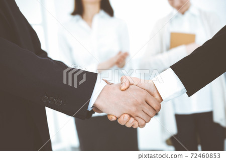 Businessman and woman shaking hands with colleagues at the background. Handshake at meeting in office. Concept of success in business 72460853