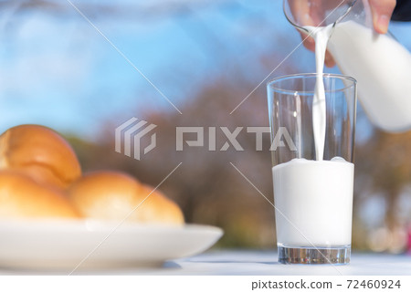 Breakfast scenery pouring milk from a pitcher into a glass on a terrace table 72460924