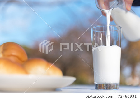 Breakfast scenery pouring milk from a pitcher into a glass on a terrace table 72460931