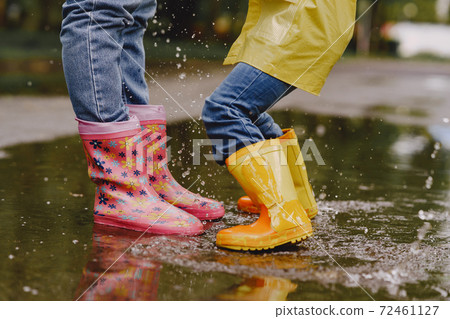 Funny kids in rain boots playing with paper ship by a puddle Funny kids in rain boots playing with paper ship by a puddle 72461127