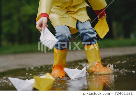 Funny kids in rain boots playing with paper ship by a puddle Funny kids in rain boots playing with paper ship by a puddle 72461181
