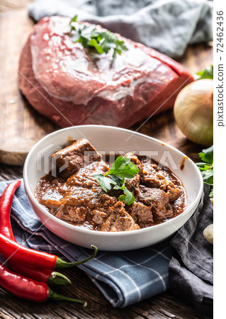 Slow stewed goulash served on a plate next to a raw piece of beef meat, onion and chillies Slow stewed goulash served on a plate next to a raw piece of beef meat, onion and chillies 72462436