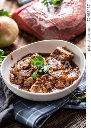 Slow stewed goulash served on a plate next to a raw piece of beef meat Slow stewed goulash served on a plate next to a raw piece of beef meat 72462437