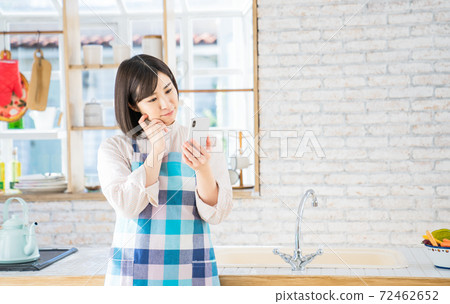 Young woman looking at her smartphone in the kitchen Young woman looking at her smartphone in the kitchen 72462652