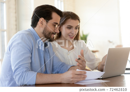 Smiling colleagues cooperate on laptop in office Smiling colleagues cooperate on laptop in office 72462810
