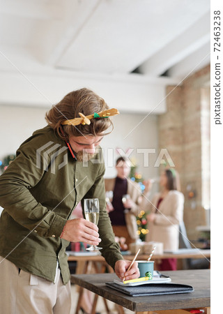 Busy young bearded man with flute of champagne talking on mobile phone Busy young bearded man with flute of champagne talking on mobile phone 72463238