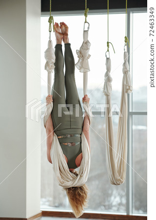 Back view of active young woman hanging upside down and holding by white hammock 72463349