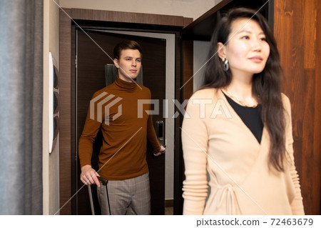 Happy young Asian woman coming out of hotel room while her husband closing door Happy young Asian woman coming out of hotel room while her husband closing door 72463679