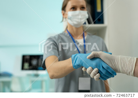 Young female clinician in protective workwear shaking hand of male colleague 72463717