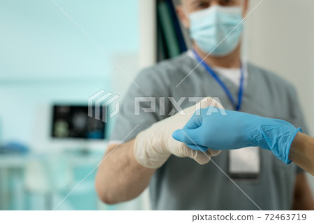 Gloved hands of two clinicians in protective workwear making punch bump 72463719