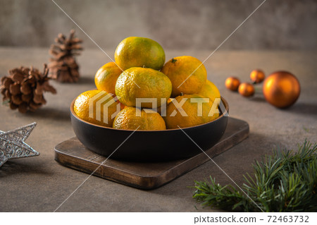 Tangerines or mandarines and ripe slices in bamboo bowl on wooden board, next to Christmas tree Tangerines or mandarines and ripe slices in bamboo bowl on wooden board, next to Christmas tree 72463732
