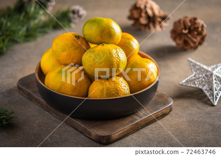 Tangerines or mandarines and ripe slices in bamboo bowl on wooden board, next to Christmas tree Tangerines or mandarines and ripe slices in bamboo bowl on wooden board, next to Christmas tree 72463746
