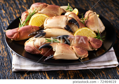 Crab claws in black plate on a wooden table, close-up. 72464619