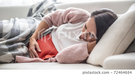 Woman falling asleep under the blanket on a couch after thermophore released the menstruation pain in her belly Woman falling asleep under the blanket on a couch after thermophore released the menstruation pain in her belly 72464684