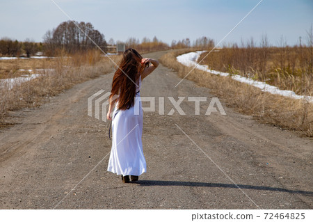 Photo of young woman in a white dress walking on a road Photo of young woman in a white dress walking on a road 72464825