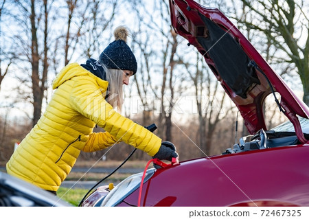 A woman is trying to connect the jumper cables in the car. A woman is trying to connect the jumper cables in the car. 72467325