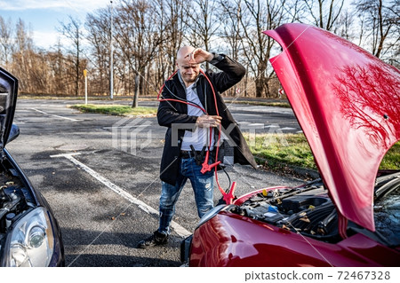 Angry driver trying to start broken car with jumper cables 72467328