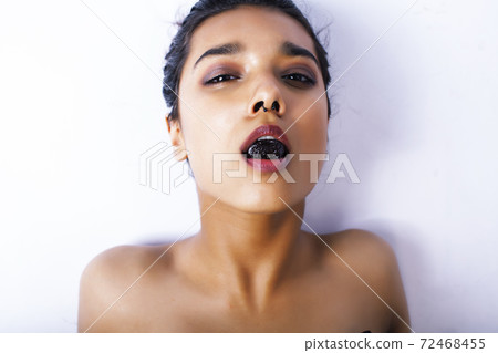 young pretty indian woman with dry fruit in mouth on white background young pretty indian woman with dry fruit in mouth on white background 72468455
