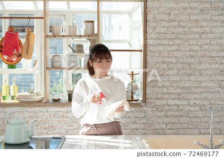 A young woman cleaning the kitchen with a rag and a spray of disinfectant 72469177