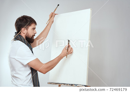 Male artist brush in hands of easel art hobby light background scarf around his neck 72469179
