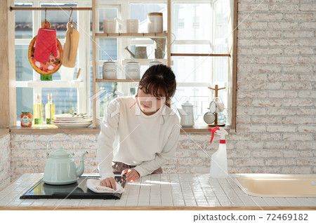 A young woman cleaning the kitchen with a rag and a spray of disinfectant 72469182