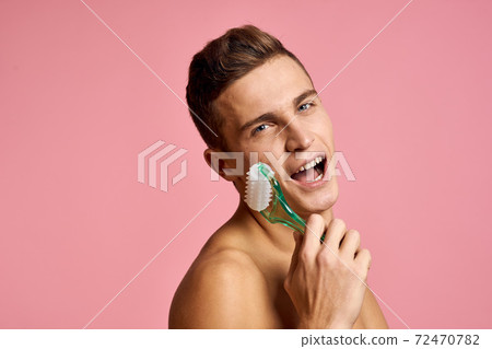Handsome man with massager in hand on isolated pink background cropped view clean skin 72470782