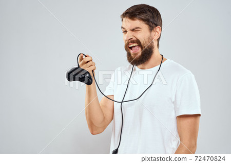 A man with a gamepad in his hands playing games leisure lifestyle technology white t-shirt light background 72470824
