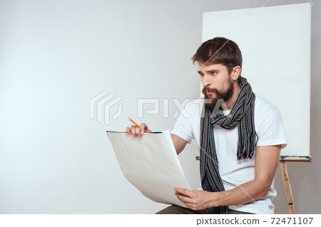 Male artist sitting on chair drawing brush easel hobby Creative light background 72471107