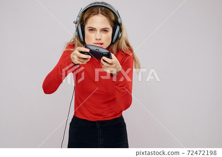 Woman with headphones Joystick in hands playing games fun leisure lifestyle entertainment red shirt gray background Woman with headphones Joystick in hands playing games fun leisure lifestyle entertainment red shirt gray background 72472198